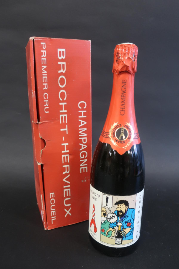 A champagne bottle with a red foil capsule beside its red presentation box: the box reads CHAMPAGNE BROCHET-HERVIEUX, PREMIER CRU, ÉCUEIL; a gold medallion on the neck carries a rocket, and the label sets the red-and-white chequered rocket beside a comic panel in which Captain Haddock opens a bottle, the cork going PAN