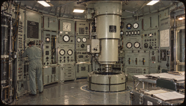 The control deck of the lunar rocket: a circular room of green instrument panels and dials around a central column, a technician in overalls at the controls
