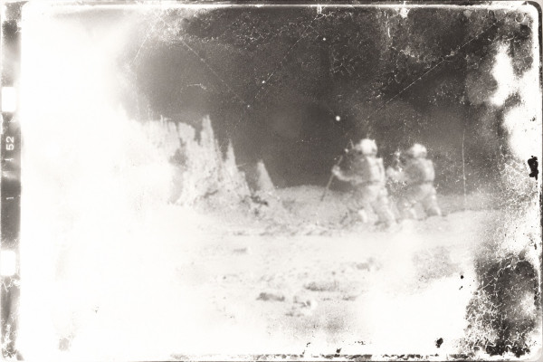 Damaged film frame: Thomson and Thompson in their space suits, hopping across the lunar ground in the low gravity, jagged rock spires to the left, half the image washed out