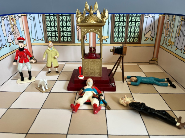 Painted metal figurines in a model of Hergé's Treasure Chamber, with frescoed walls, barred windows and a chequered floor: the gilded case with the crown on a red dais, a bellows camera on its tripod and the magnesium powder; Tintin, Snowy and a man in a red tunic stand on the left, while a guard, Czarlitz and the Professor lie on the floor