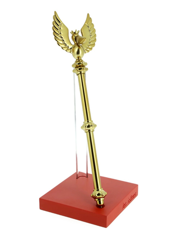 A gilt replica of the sceptre topped by a crowned pelican with raised wings, held upright by a clear support on a red base engraved “les icônes”, on a white background