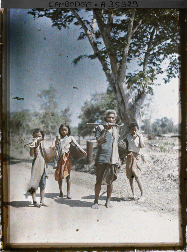 Autochrome of man carrying palm juice and children with baskets on road near Siem Reap