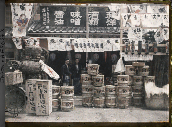 Autochrome of grocers at shop entrance in Tokyo displaying barrels of beer miso and sake